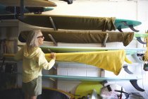 Senior woman taking surfboard from shelf — Stock Photo