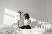Chica dando ayuda mano a hembra niño hermana a toddling en cama - foto de stock