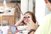 Батько і дочка сидять за столом сніданку, дочка робить бінокль з пальців — стокове фото