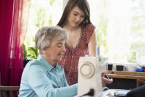 Внучка наблюдает за бабушкой с помощью швейной машинки — стоковое фото