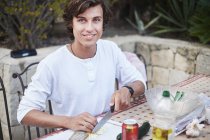 Junger Mann schneidet Brot am Terrassentisch — Stockfoto