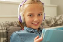 Chica con auriculares sosteniendo la tableta digital mirando a la cámara sonriendo - foto de stock
