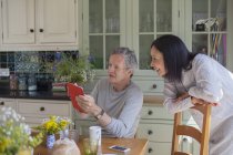 Senior couple in kitchen, looking at digital tablet — Stock Photo