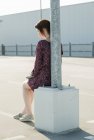 Молода жінка сидить, спираючись на лампу на порожній парковці — стокове фото