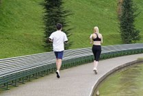 Man and woman running beside lake, rear view — Stock Photo