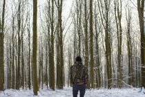 Vista posteriore del giovane in piedi nella foresta innevata con alberi nudi — Foto stock