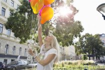 Mature woman, outdoors, holding bunch of balloons — Stock Photo