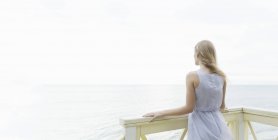 Vista trasera de la mujer joven mirando hacia el mar desde el balcón, Miami Beach, Florida, EE.UU. - foto de stock