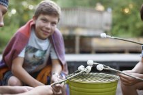 Group of pre-adolescent boys toasting marshmallows over bucket barbecue — Stock Photo