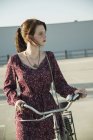Young woman pushing bicycle in empty parking lot — Stock Photo
