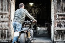Вид ззаду людини штовхає мотоцикл в сарай — стокове фото