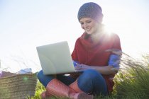 Молода жінка використовує ноутбук, сидячи в довгій траві — стокове фото