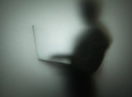 Silhouette de la personne utilisant un ordinateur portable, derrière le verre — Photo de stock
