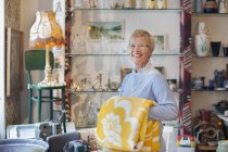 Портрет зрелой женщины, складывающей желтое одеяло в винтажном магазине — стоковое фото