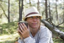Зріла жінка в федорі п'є чай в лісі — стокове фото