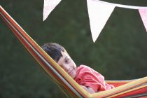 Retrato de menino bonito reclinado em rede de jardim listrado — Fotografia de Stock