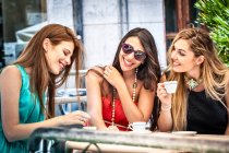 Three young female friends drinking espresso at sidewalk cafe, Cagliari, Sardinia, Italy — Stock Photo