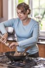 Середня доросла жінка поливає олію, щоб прокинутися на кухні — стокове фото