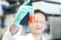 Молода жінка лабораторії технік притримуючи помаранчевий зразка в лабораторії — стокове фото