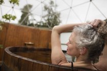 Зріла жінка з руками в волоссі в гарячій ванні на еко-відступ — стокове фото