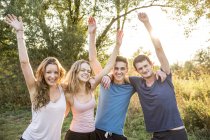 Portrait of group of friends in rural environment, arms raised, smiling — Stock Photo