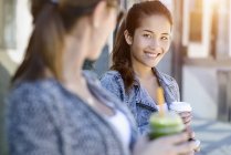 Two young women with takeaway coffee leaning against park building — Stock Photo