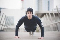 Young male runner doing press ups on city footbridge — Stock Photo