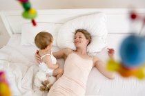 Mother and baby daughter lying on bed, high angle — Stock Photo