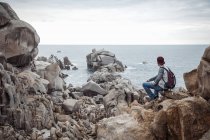 Veduta posteriore del giovane seduto sulle rocce guardando l'oceano, Costa Smeralda, Sardegna, Italia — Foto stock