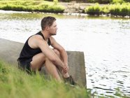 Joven en deportes sentado en la orilla del río - foto de stock