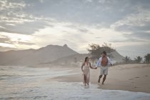 Середня доросла пара біжить уздовж пляжу, рука в руці — стокове фото