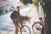 Young man carrying bunch of sticks on bicycle — Stock Photo