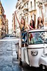 Три молодих жінок розмахуючи від відкритої задньої сидіння італійського таксі, Кальярі, Сардинія, Італія — стокове фото