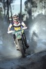 Young male motocross racer splashing through forest puddle — Stock Photo
