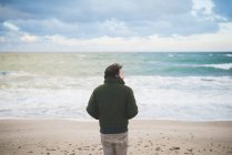 Vista trasera del hombre mirando hacia los lados en la playa ventosa, Sorso, Sassari, Cerdeña, Italia - foto de stock