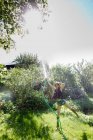 Вид спереду зріла жінка в саду стоїть на одній нозі бризкає воду в повітря з шлангом — стокове фото
