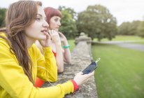 Young woman with smartphone leaning against stone wall — Stock Photo