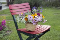 Fresh cut flowers in straw hat, on garden chair — Stock Photo