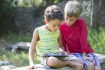 Two boys sitting on garden seat looking down at digital tablet — Stock Photo