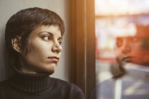Portrait of young woman looking out of window at street — Stock Photo