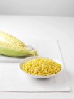 Raw corncobs on marble cutting board and bowl of boiled sweetcorn — Stock Photo