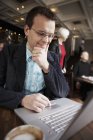 Empresário usando laptop no interior do café com pessoas em segundo plano — Fotografia de Stock