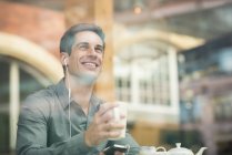 Jovem empresário ouvindo fones de ouvido no assento da janela do café, Londres, Reino Unido — Fotografia de Stock