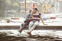 Couple sitting on pier whispering and eating ice cream cone at lake Mergozzo, Verbania, Piemonte, Italy — Stock Photo