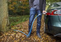 Homem cobrando carro elétrico na floresta de outono — Fotografia de Stock