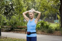 Зрелая женщина, завязывающая волосы во время тренировки в парке — стоковое фото