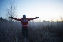 Человек с распростертыми руками на солнечной сельской зимней сцене — стоковое фото