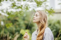 Young woman in field holding up a stem of long grass — Stock Photo