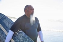 Maduro surfista masculino passeando na praia com prancha — Fotografia de Stock