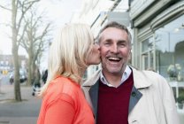 Mujer besando novio en mejilla en pueblo calle - foto de stock
